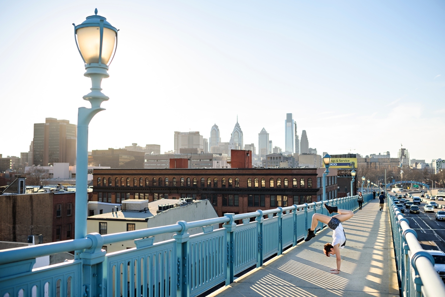 A woman on the walkway of Ben Franklin Bridge doing a handstand with the Philadelphia skyline in the background.